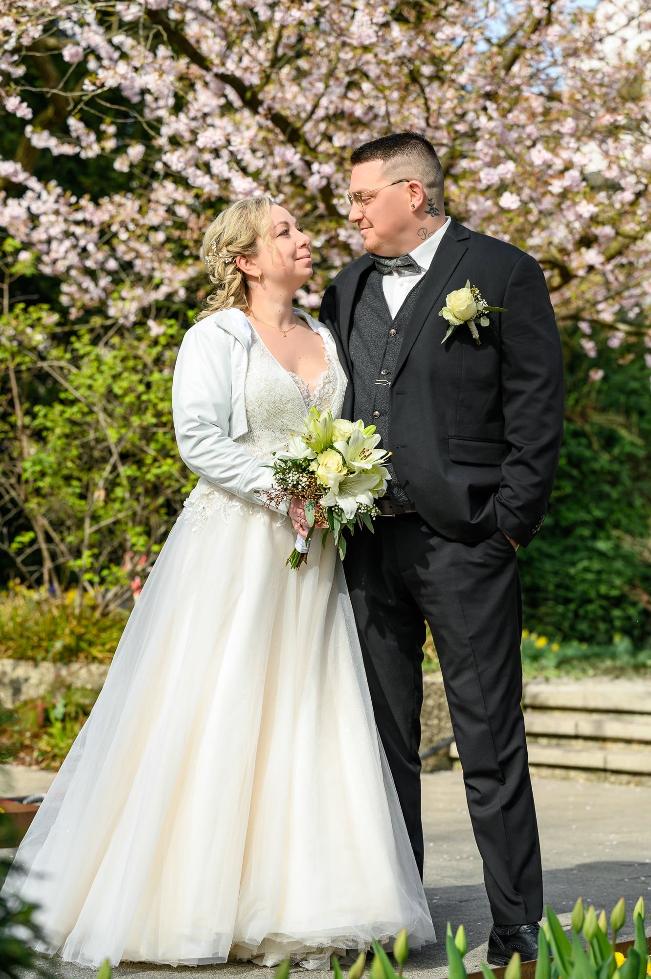 Brautpaar schaut sich vor einem blühenden Kirschbaum an, die Braut mit hellem Brautstrauß – Hochzeit in Augsburg